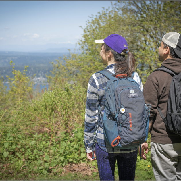 Two hikers in green park looking out at water view.