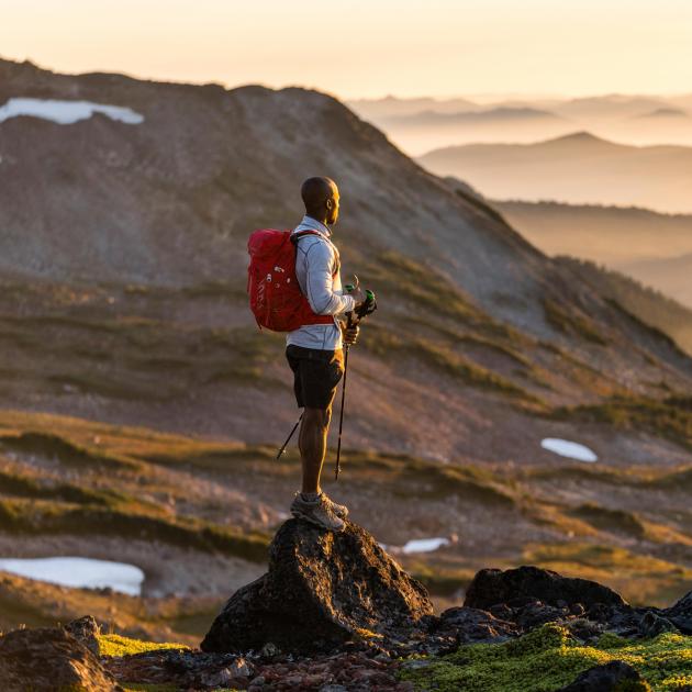 Lone hiker facing rays of sun in front of mountainous landscape in Mount Rainier National Park, Washington