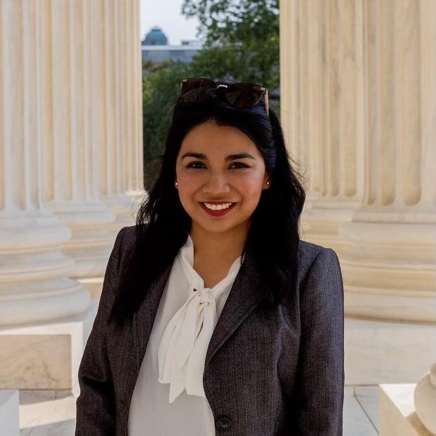 a woman in a suite is standing outdoors between two columns 