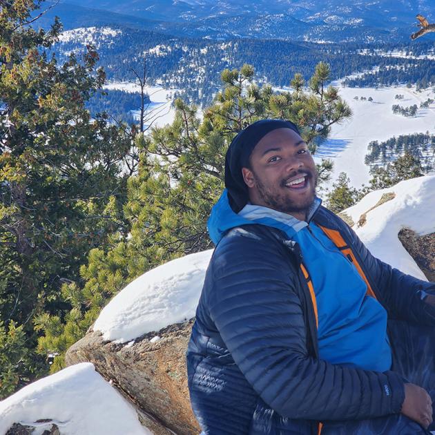 person smiling at camera with mountains and snow in the background