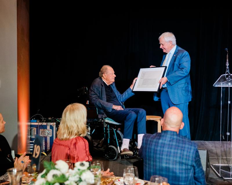 person giving award to person on a wheelchair, on a stage 