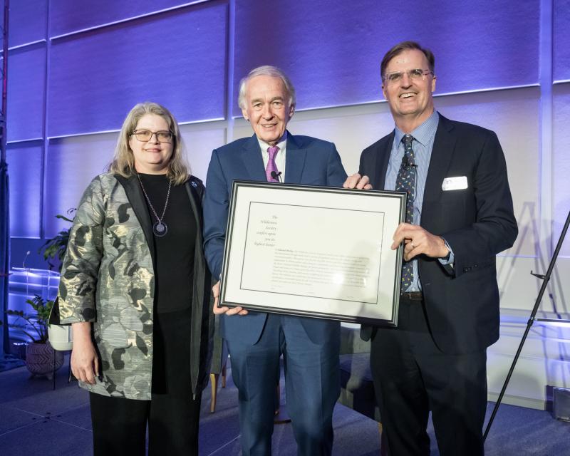 Three people standing together and holding a framed certificate