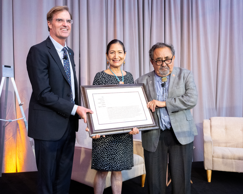 three people stand next to each other with the woman in the middle holding a certificate 