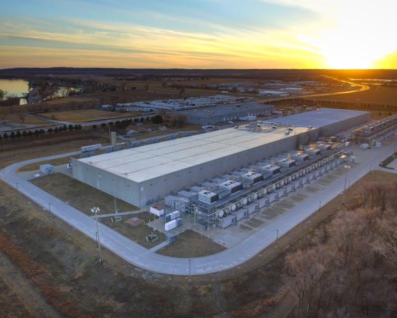 Warehouse-like building near body of water with sun shining on the horizon