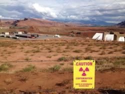 Sign reads "CAUTION - contamination area" in foreground of industrial site at the Moab Uranium Mill Tailings Remedial Action (UMTRA) project in Moab, Utah